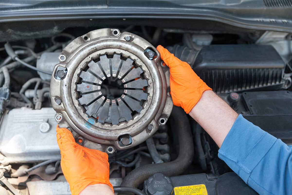 Auto mechanic wearing protective work gloves holding used clutch pressure plate