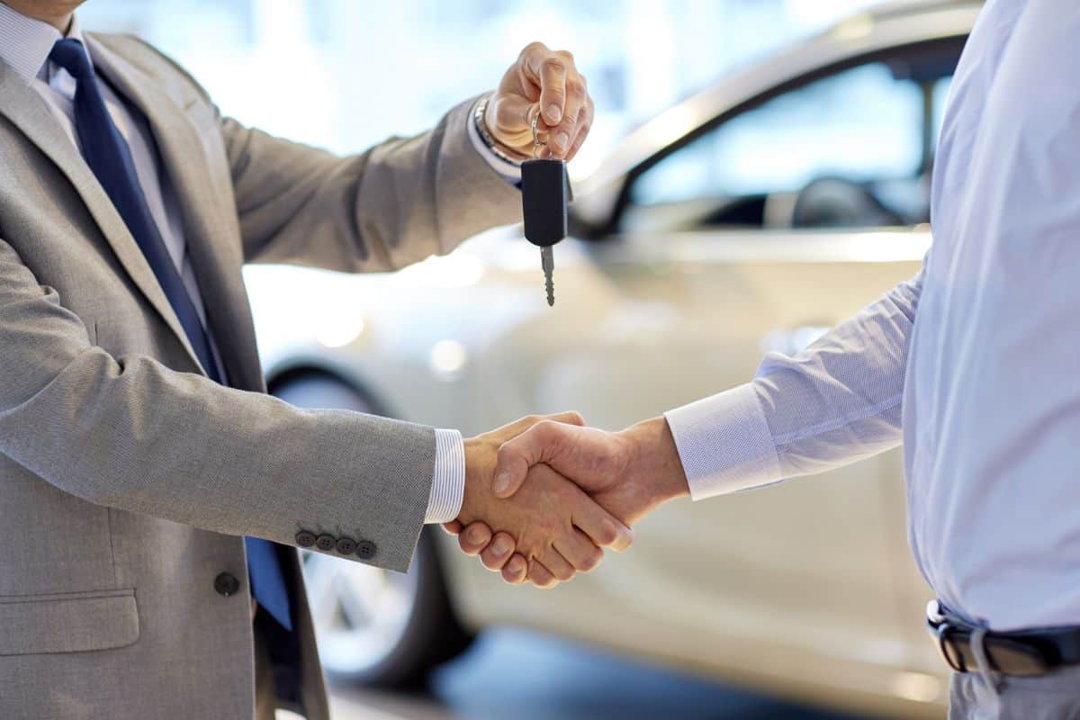 auto business, car sale, deal, gesture and people concept - close up of dealer giving key to new owner and shaking hands in auto show or salon