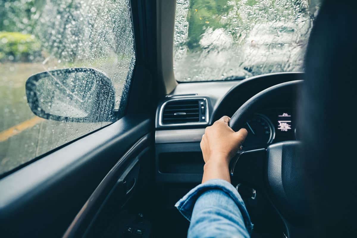 photo of a woman driving a car, holding steering wheel, heavy rain outside