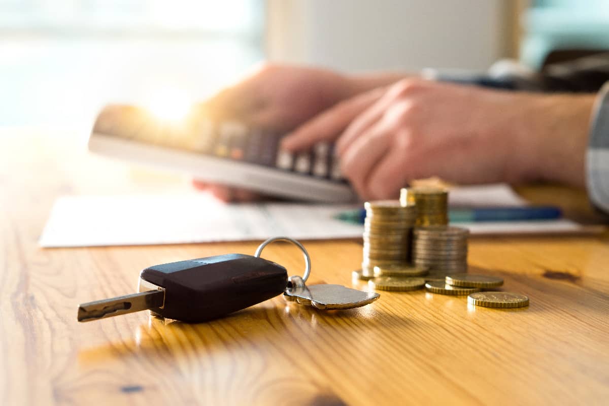Car keys and money on table with man using calculator