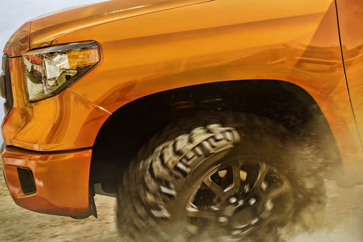 Moving offroad orange Toyota Tundra wheel and bumper view.