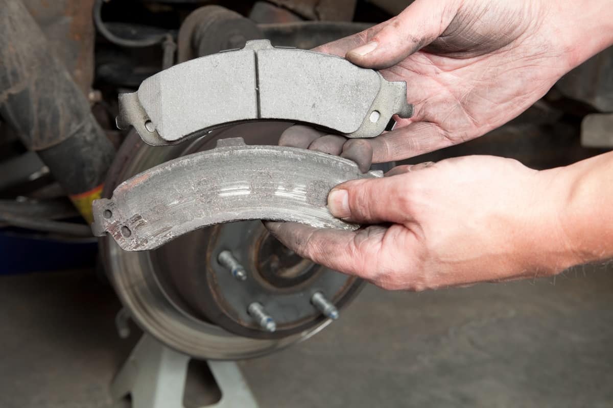 Worn Brake Pads - A mechanic's hands are displaying a worn to the metal brake pad (lower) and a new pad (upper).