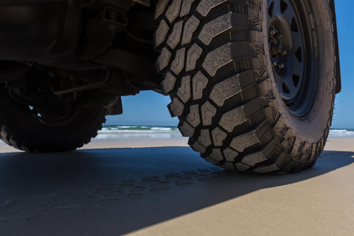 close up car vehicle off road wheels and tires on the sand of the sea shore
