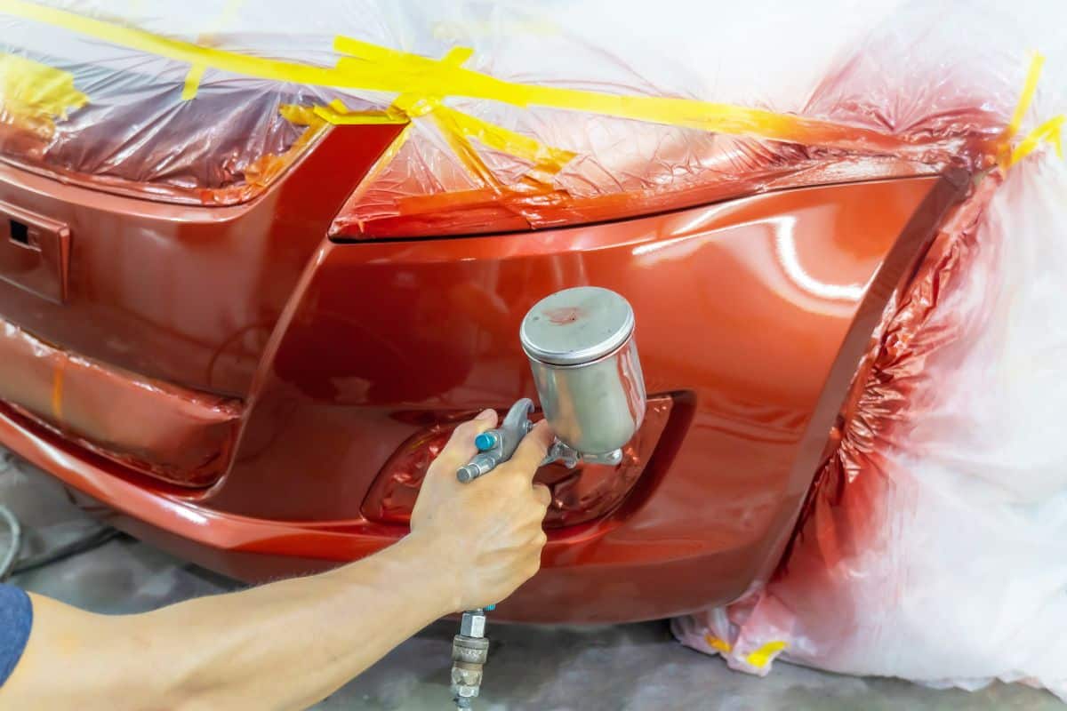 spray gun with paint for painting a car ,Man with protective clothes and mask painting car using spray compressor.