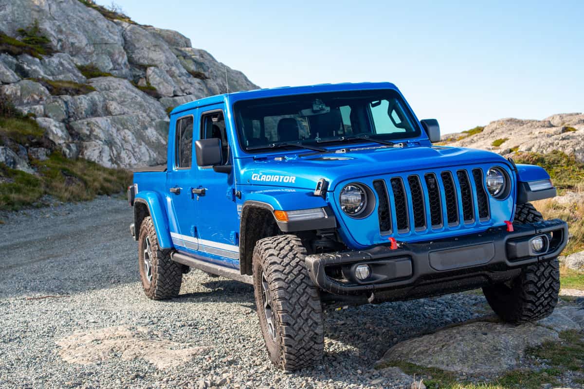 A vibrant blue Jeep Gladiator Rubicon truck 4x4 off road and parked on the side of a hill with the blue ocean