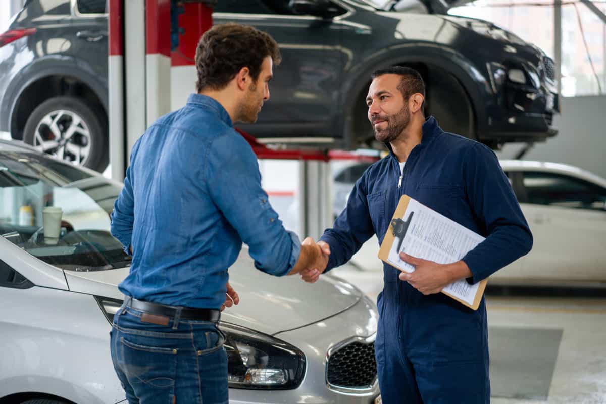 Latin American man greeting a mechanic with a handshake while picking up his car at an auto repair shop.