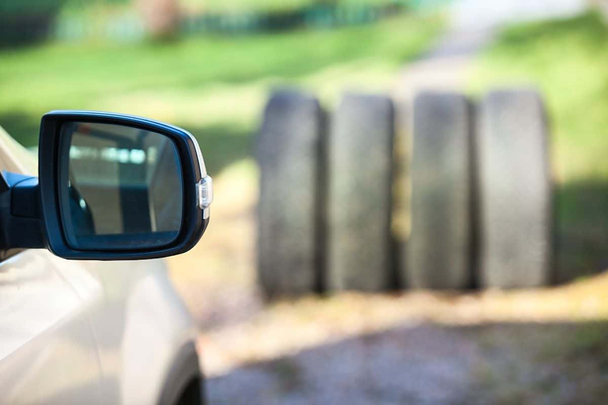 Side mirror of car against four tyres, seasonal wheel and tire changing concept