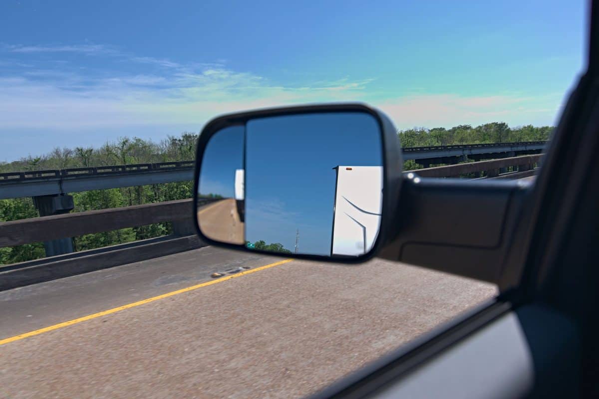 Truck towing trailer view from side mirror. Pulling rv down highway with diesel using tow mirrors to see travel trailer behind.