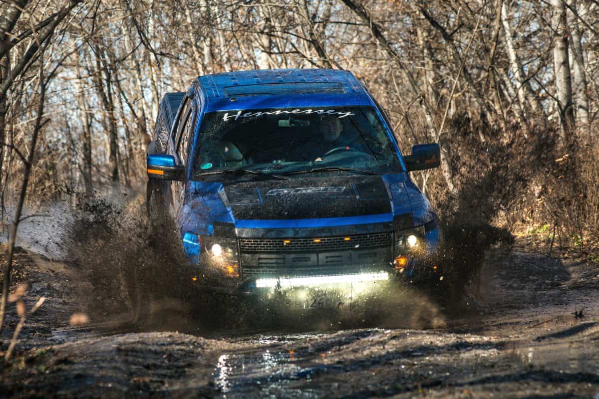 Ford F150 Raptor SUV is on the road driving on dirt . pickup