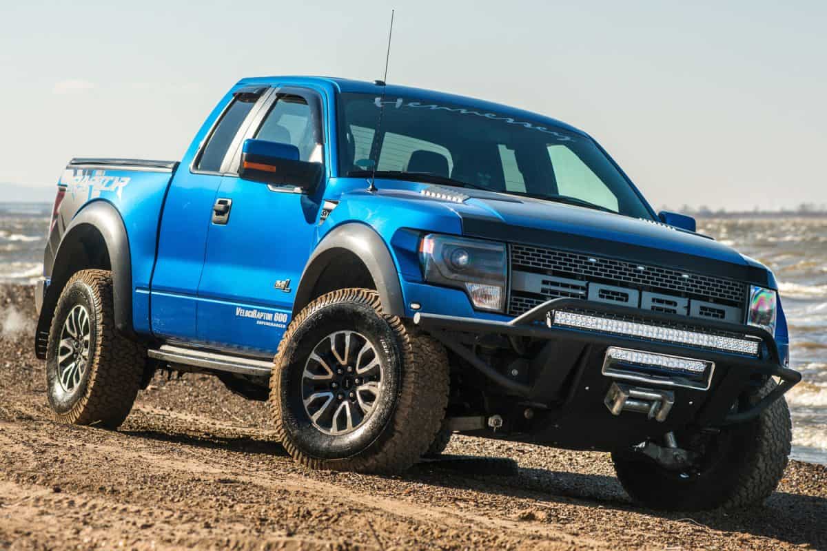 Ford F150 Raptor SUV is on the road driving on dirt . pickup