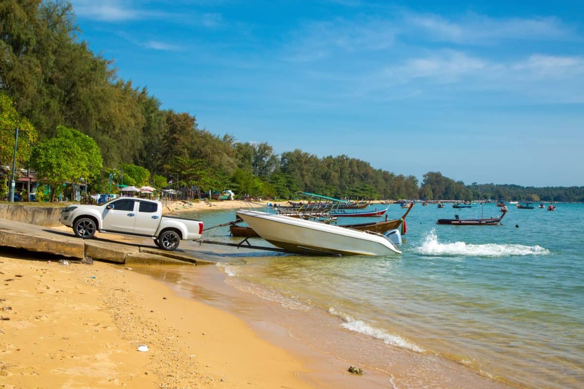 Lifting a boat from the sea with a pickup truck. Low tide at the Rawai beach on the background of longtail fishing boats and speedboats.